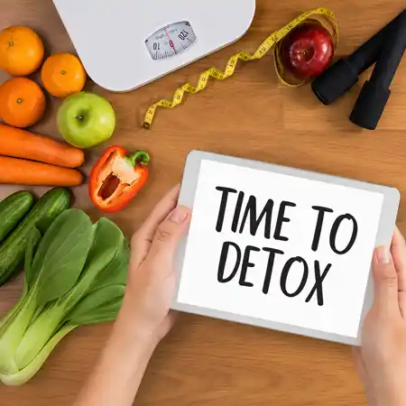 Hands hold a tablet displaying text next to fresh vegetables fruits and fitness equipment.