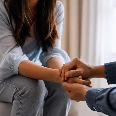 Two people hold hands in a supportive gesture during a mental health counseling therapy session.